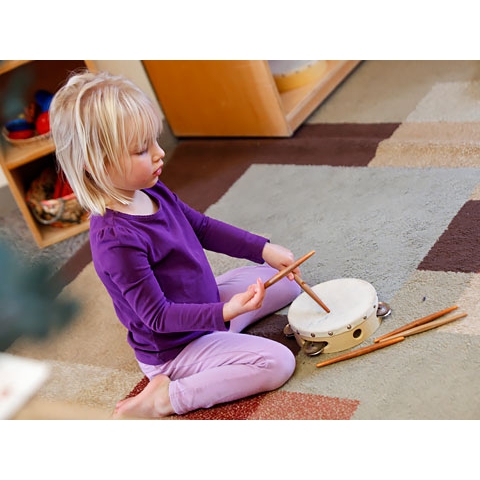 Child playing with drum sticks and tambourine in music area