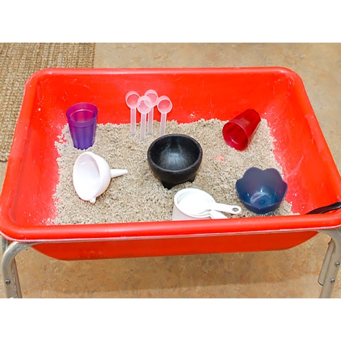 Open container with sand, cups, funnel, and measuring spoons