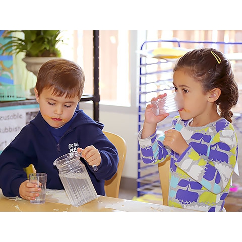 Two children at table pouring and drinking water